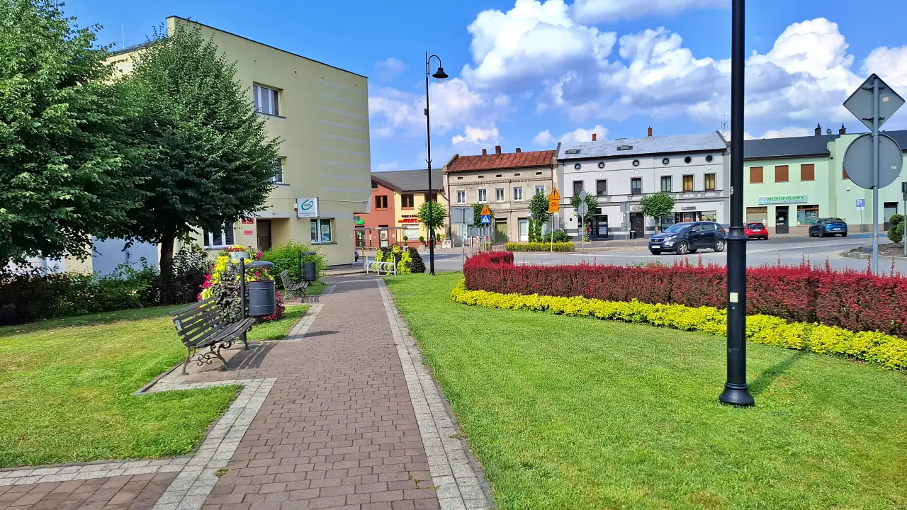 Zadbana przestrzeń publiczna w centrum Kobylej Góry z alejką, zielenią i miejscami do odpoczynku.