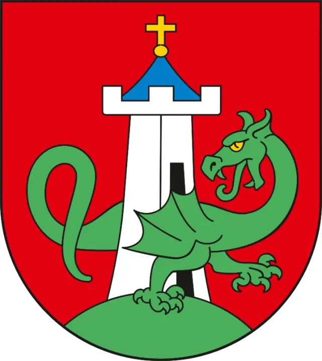 Herb Żmigrodu przedstawiający srebrną wieżę z błękitnym dachem zwieńczonym złotym krzyżem oraz zielonego skrzydlatego smoka przechodzącego przez bramę.
