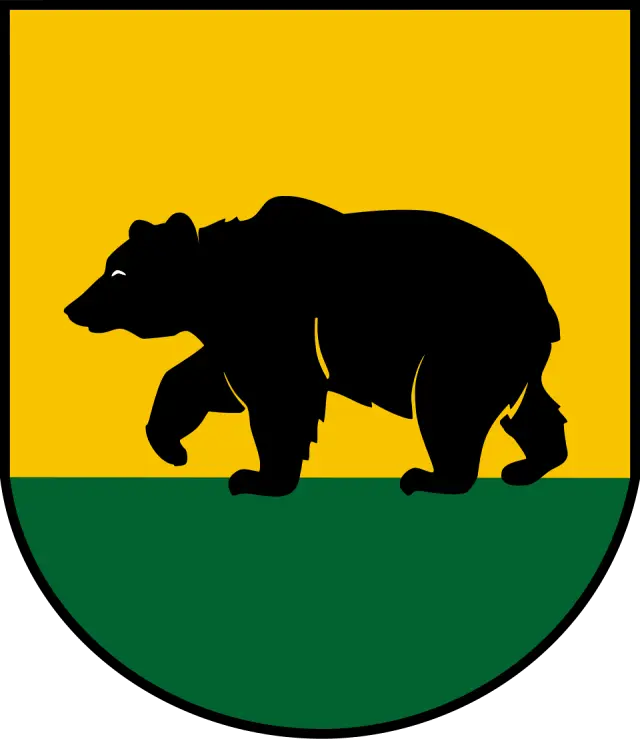 Herb Rawicza przedstawiający czarnego niedźwiedzia z uniesioną prawą przednią łapą na zielonej murawie