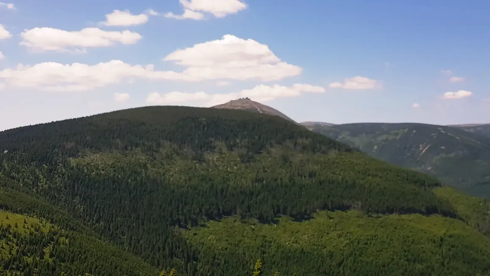 Panorama Karkonoskiego Parku Narodowego z widokiem na Śnieżkę, najwyższy szczyt Sudetów, otoczony górskimi lasami i grzbietami Karkonoszy.